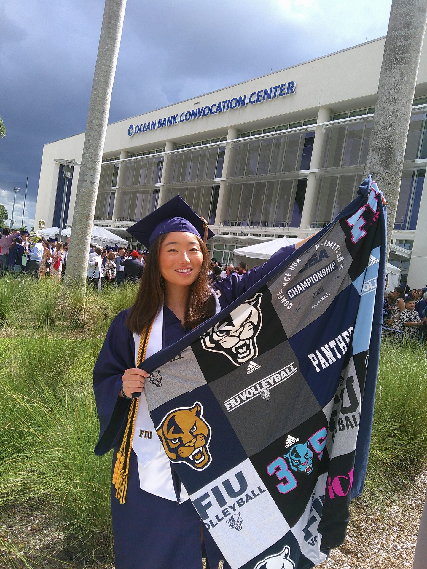 FIU college graduate in cap and gown holding custom Project Repat volleyball t-shirt quilt at graduation ceremony