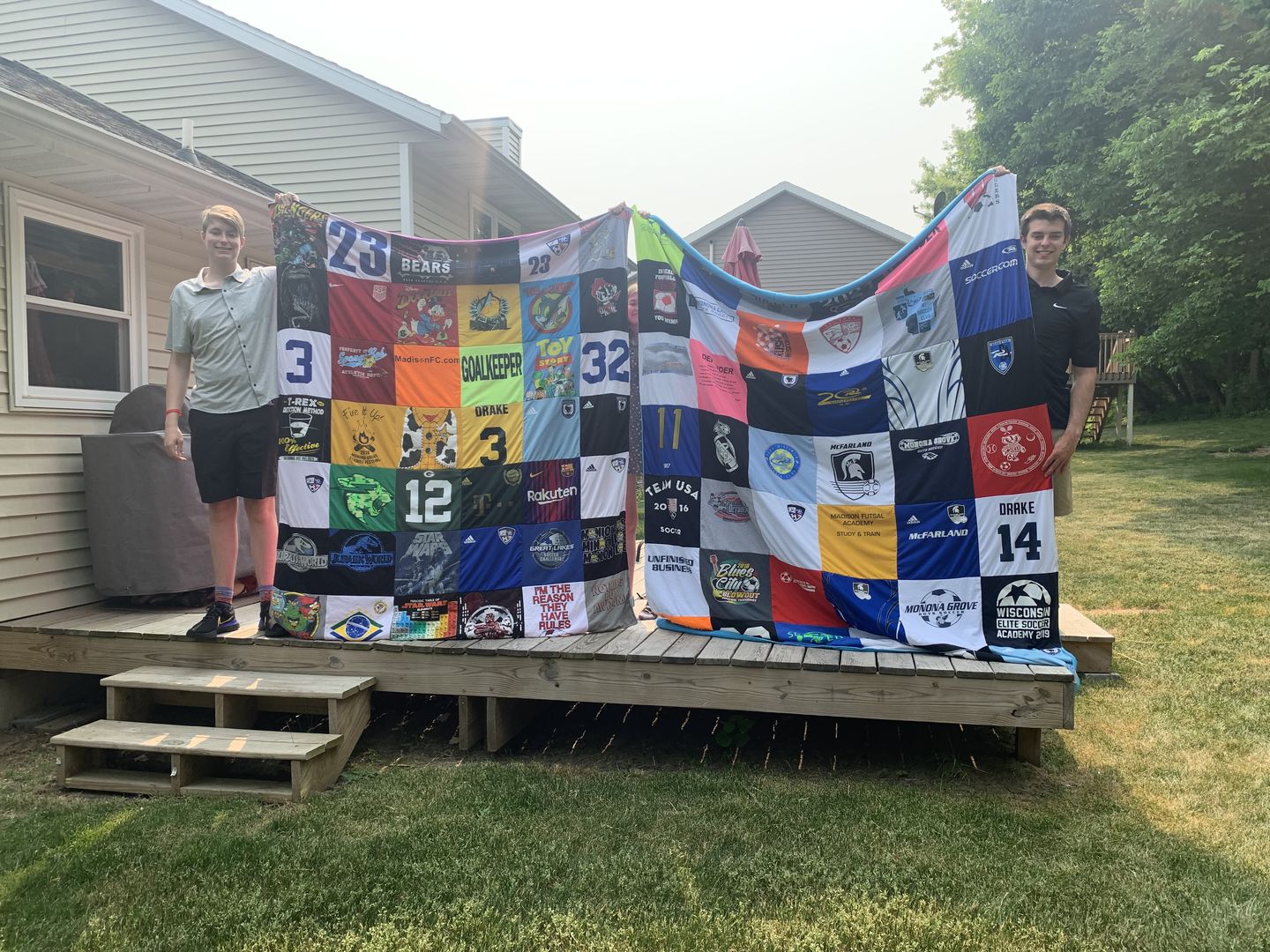 Two high school graduates holding large custom Project Repat t-shirt quilts outdoors at graduation